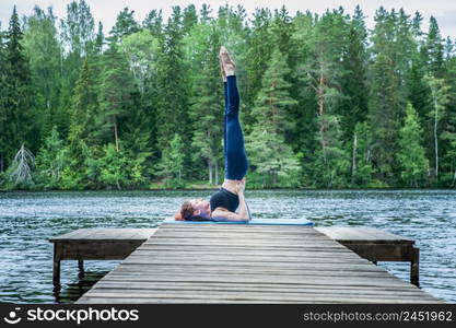 Young yogi girl practicing yoga, standing in Salamba Sarvangasana exercise, supported Shoulder stand pose on the lake. Concept of healthy life and natural balance