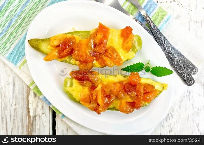 Young zucchini baked in a flavored sauce with dried apricot, cream and cheese in a bowl on a towel on the background of the wooden planks on top