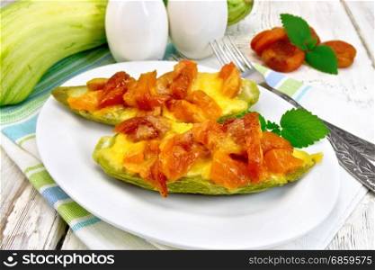 Young zucchini baked in a flavored sauce with dried apricot, cream and cheese in a bowl on a kitchen towel on the background of wooden boards