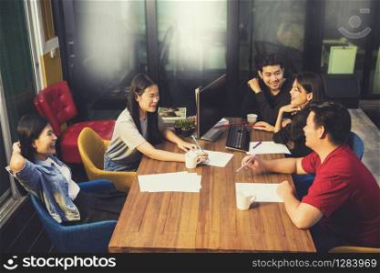 younger asian freelance team relaxing on working table in office meeting room