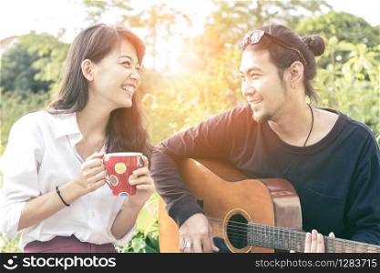 younger asian man and woman relaxing playing guitar in park