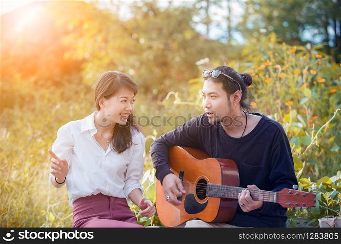 younger asian man and woman relaxing playing guitar in park