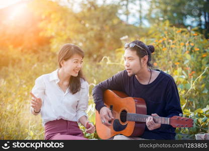 younger asian man and woman relaxing playing guitar in park