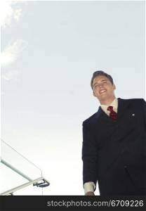 Younger business man in black suit and red tie smiles as he stands holding his briefcase walking down steps