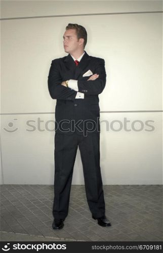 Younger business man in black suit in red tie standing in dynamic pose in front of metallic background