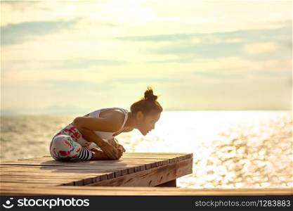 younger woman playing yoga pose on beach pier