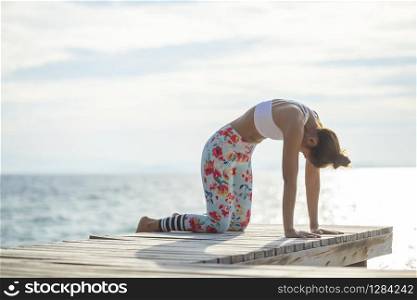 younger woman playing yoga pose on sea pier