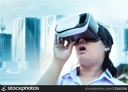 younger woman wearing virtual reality glasses with surprising face standing outdoor against modern city building background