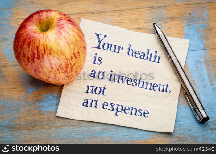 Your health is an investment, not an expense - wellness concept - handwriting on a napkin with a fresh apple