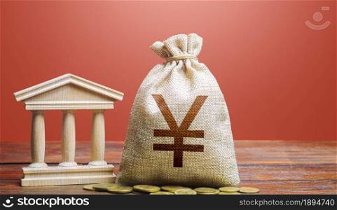 Yuan or Yen money bag and bank / government building. Monetary policy. Tax collection and budgeting. GDP and GNP. Support businesses in times of crisis. Lending loans, deposits. State debt.