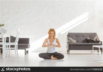 Yuong woman sitting on the floor in yoga pose, living room interior in white tones on background. Female person doing morning exercise, meditation. Yuong woman sitting on the floor in yoga pose
