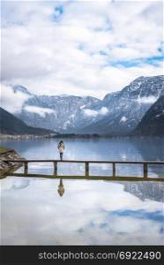 Zen moments theme image with a woman standing alone on a bridge over the Hallstatter lake, surrounded by silence and the Dachstein mountains, in Austria.