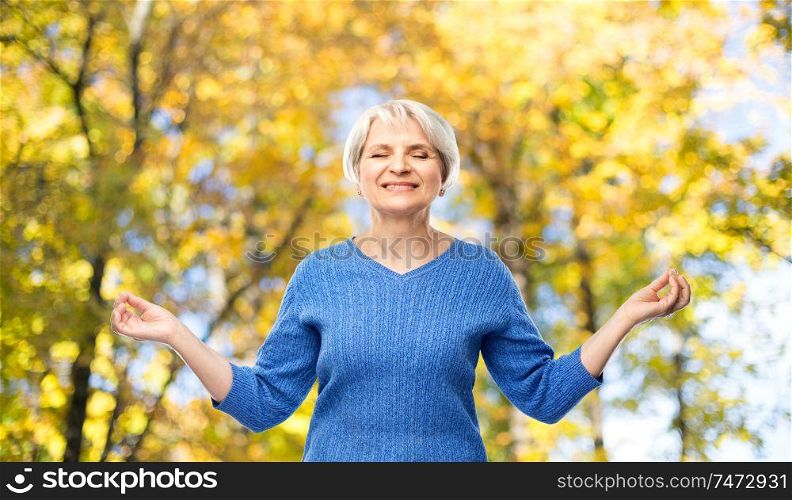 zen, relax and old people concept - portrait of smiling senior woman in blue sweater chilling over autumn park background. smiling senior woman chilling in autumn park