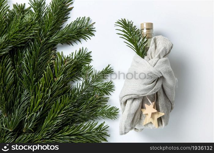 Zero waste Merry Christmas winter gift wrapping, bottle in Japanese furoshiki style in linen fabric, decorated with natural green branches of fir nobilis. Concept eco-friendly creative package.