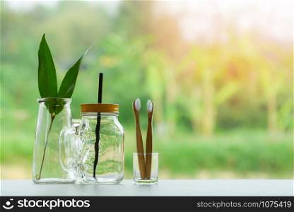 Zero waste use less plastic concept / eco green leaf in water glass jar with straw pitcher vase and bamboo toothbrush free plastic on nature environment background