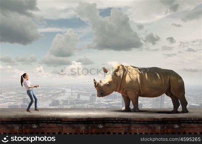 Zoo animal. Young scared woman holding rhino on rope