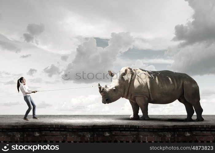 Zoo animal. Young scared woman holding rhino on rope