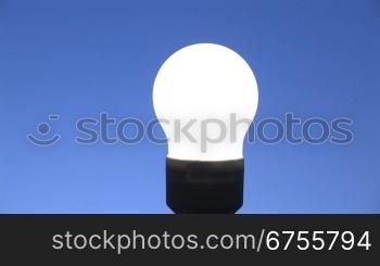 Zoom auf eine leuchtende Energiesparlampe, blauer Hintergrund