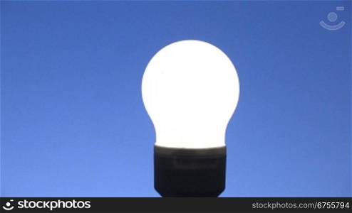 Zoom auf eine leuchtende Energiesparlampe, blauer Hintergrund