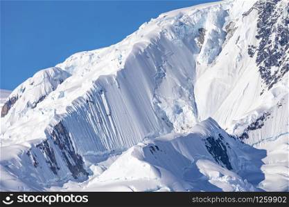 Zoom of mountain peaks covered with ice and snow against a blue sky in Antarctica
