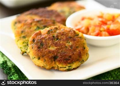 Zucchini, couscous and parsley fritters with tomato and onion dip on the side, photographed with natural light (Selective Focus, Focus in the middle of the first fritter)