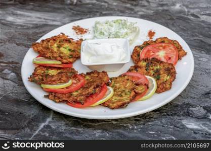 Zucchini hash or Turkish kabak mucver with yoghurt and tomatoes on a white plate