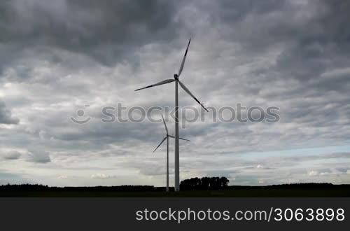Zwei Windanlagen sind vor eindrucksvollem Himmel in Bewegung